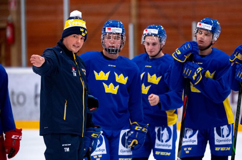 Tre unga killar i hockey utrustning lyssnar på sin tränare