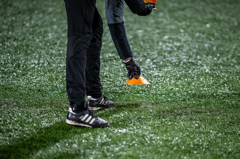 Idrottsledare sätter ner koner i marken på en fotbollsplan.