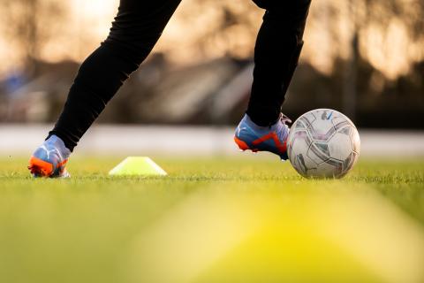 En spelare med boll driver förbi en gul kona under en fotbollsträning.