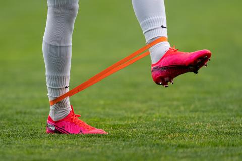 Fotbollsspelare rehabtränar med orange gummiband. 