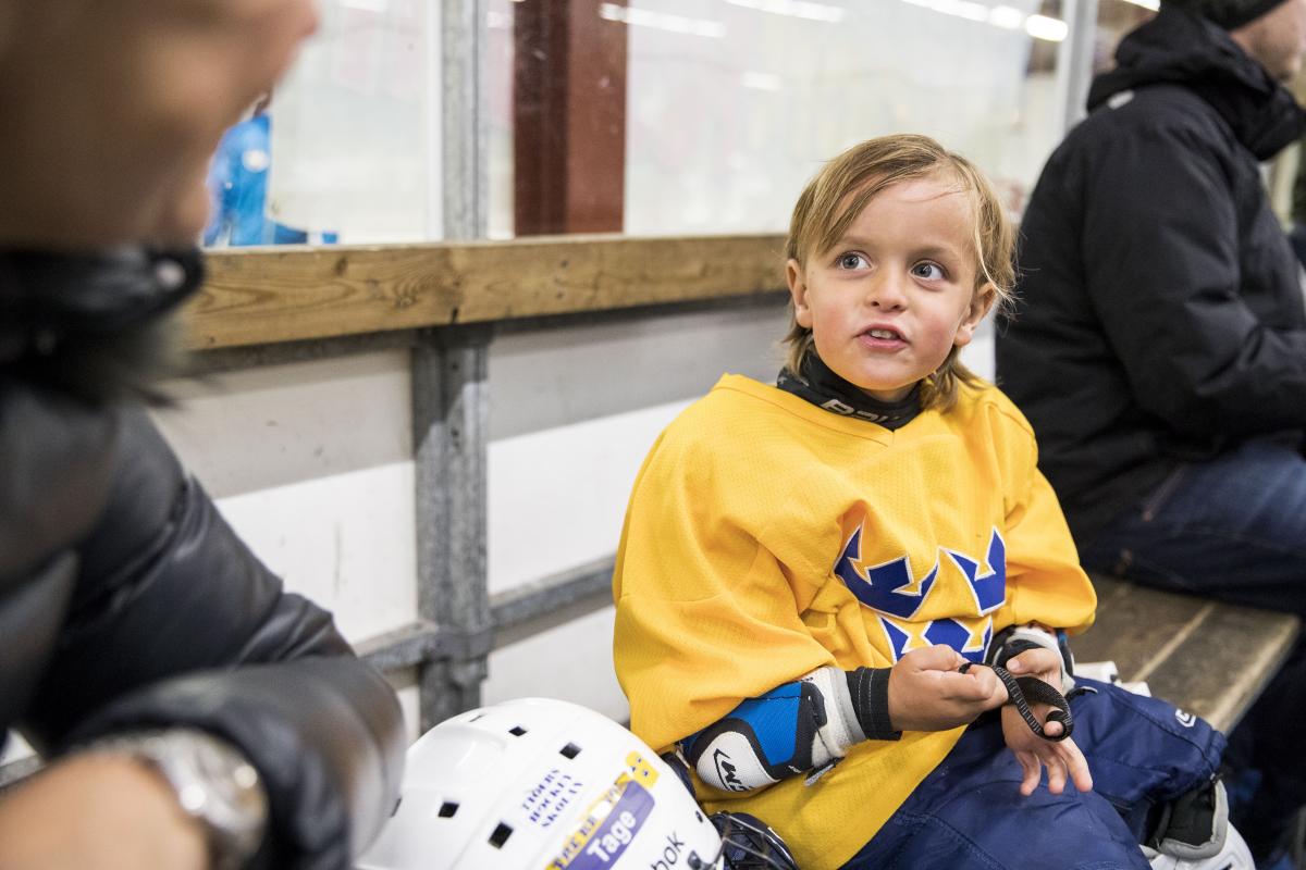 Ung pojke i hockeymundering som sitter på avbytarbänken