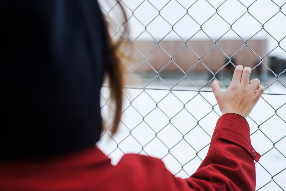 Ett barn kikar genom ett staket in till en idrottsplats.