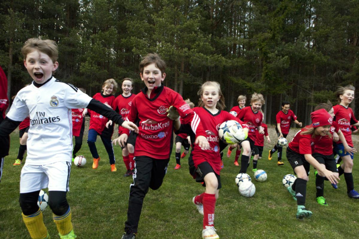 Springande barn i idrottskläder på ett grönt fält