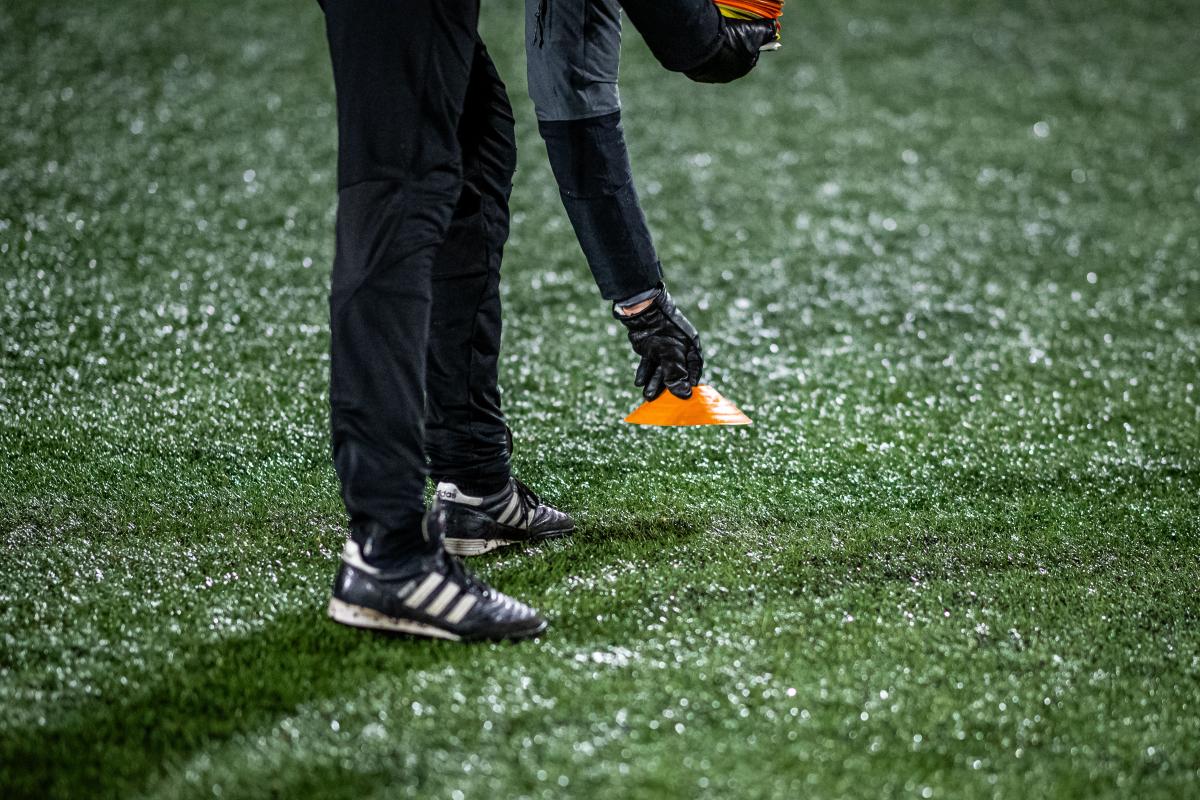 Idrottsledare sätter ner koner i marken på en fotbollsplan.